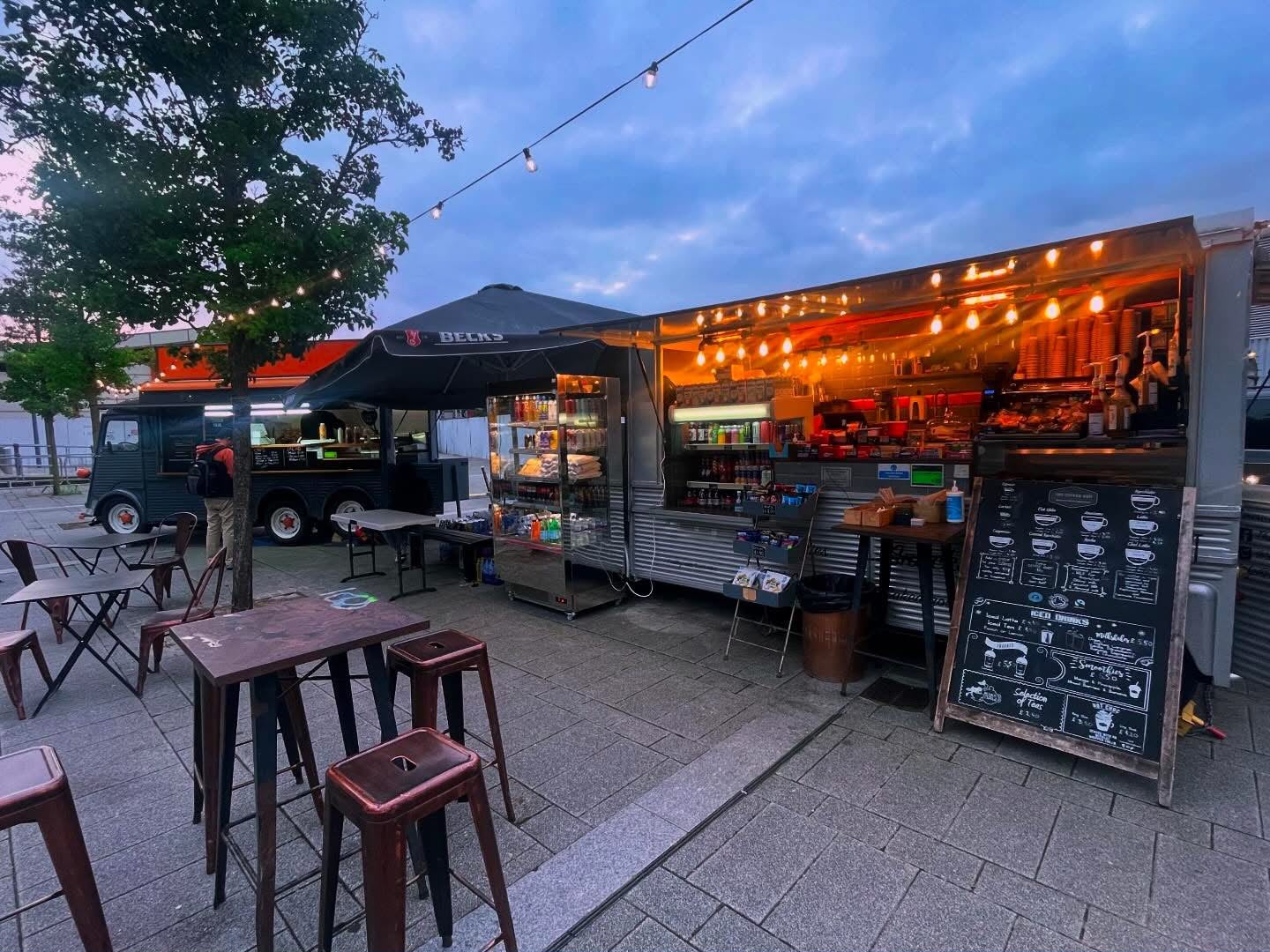 Coffee van and seating area lit with string lights at dusk